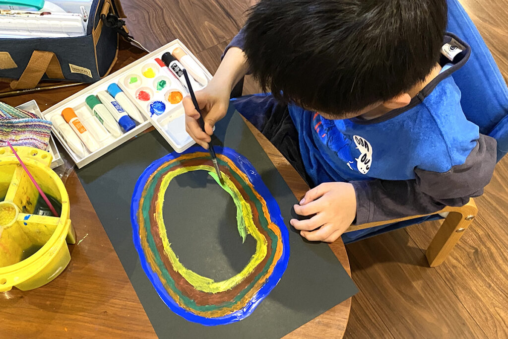 黒い画用紙にカラフルな円を描く子ども（AKASHI）の姿