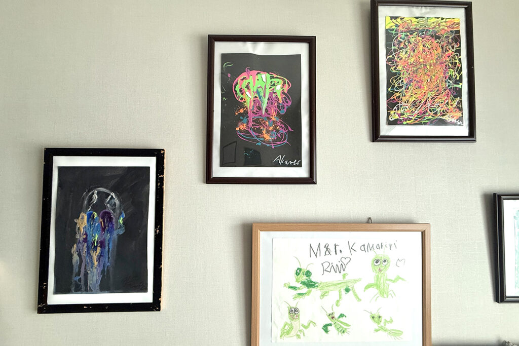 黒い画用紙に描かれたAKASHIのアート作品が額装され、白い壁に飾られている様子。下には妹RIRIのカマキリの絵も並んでいる。