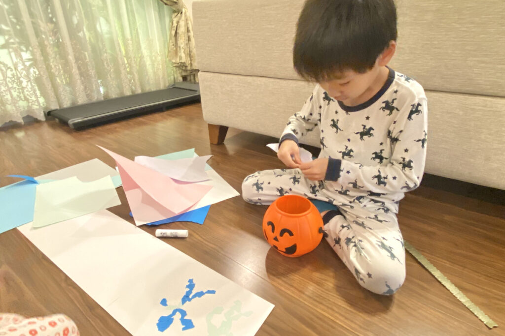 床に広げた色画用紙を前に、パジャマ姿で紙をちぎっている男の子