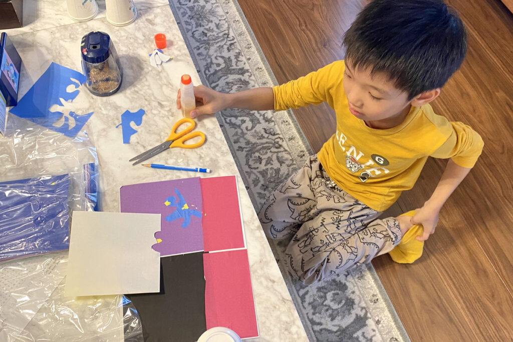 紫や赤の色紙の上に青い人型パーツを貼りながら、切り絵を制作する男の子