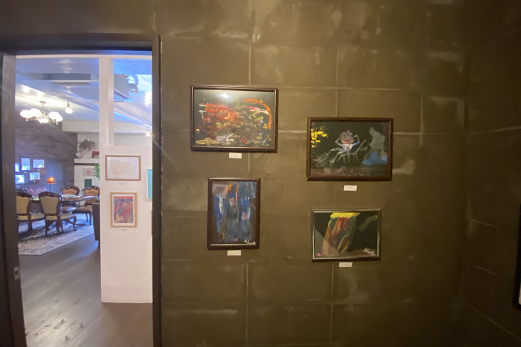 黒い壁に展示されたAKASHIのアート作品。額に入れられた黒い画用紙の作品が並び、落ち着いた照明のギャラリー空間が広がる。