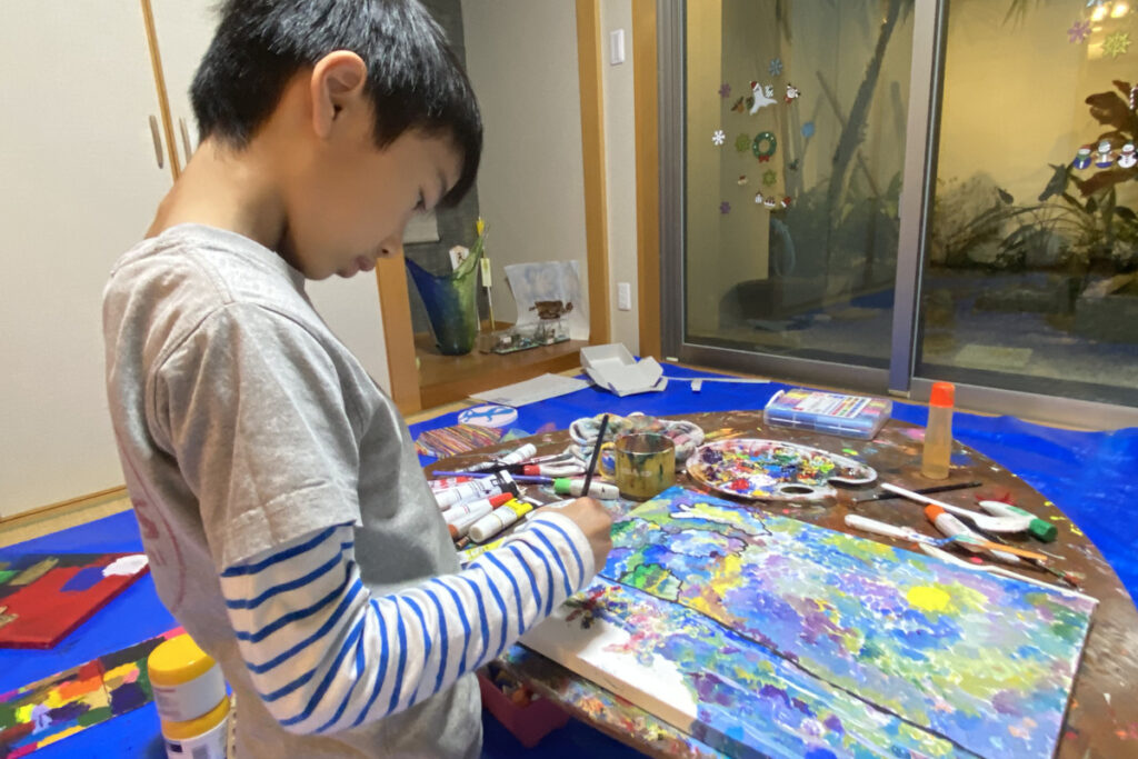 自由に絵を描くAKASHIと、絵の具で彩られた机