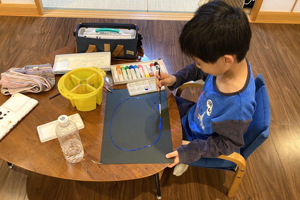 黒い画用紙に青い絵の具で円を描く男の子