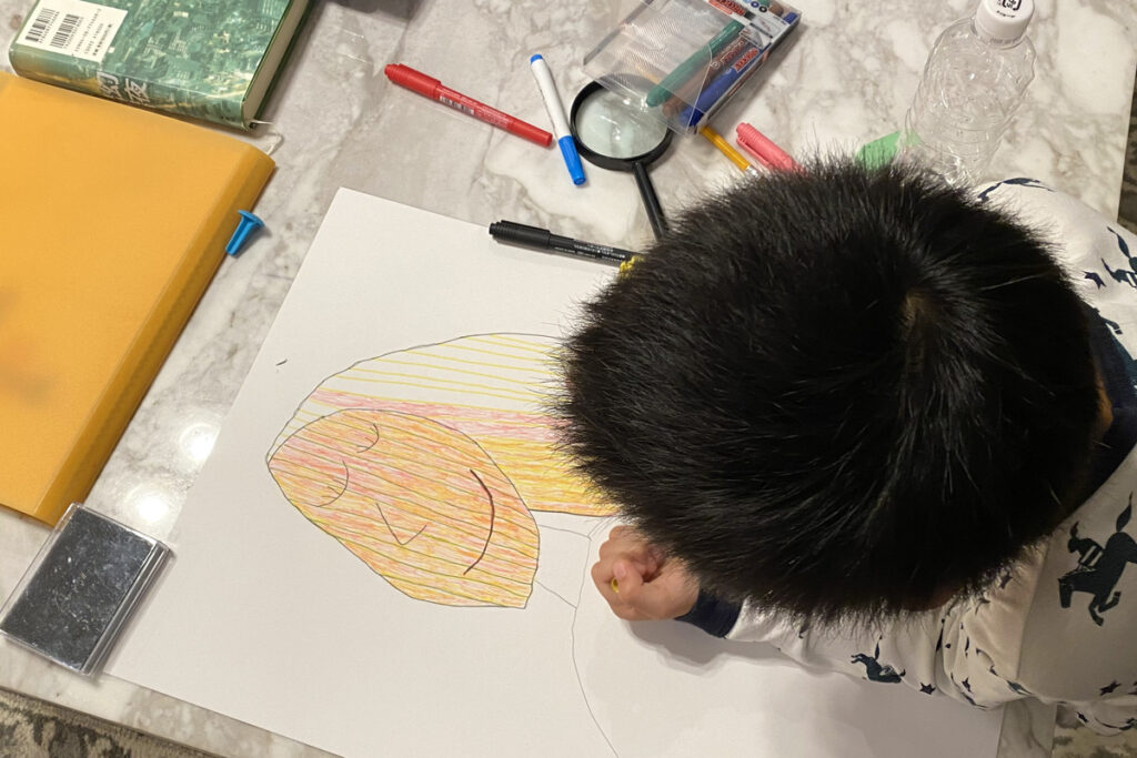 机いっぱいに画材を広げて絵を描くAKASHIの後ろ姿