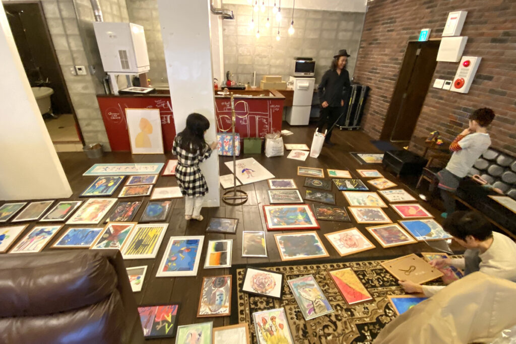 床一面に作品を並べ、家族や仲間と一緒に展示準備をする様子