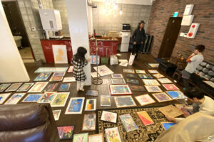 床一面に作品を並べ、家族や仲間と一緒に展示準備をする様子