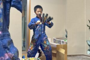 絵の具でカラフルになったつなぎを着て笑顔を見せるAKASHI