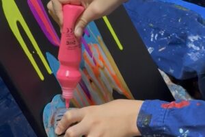 黒いキャンバスに蛍光ピンクの絵の具を丁寧に垂らすAKASHI(9歳)の手元。
重なり合う色がとろけるように混ざっていく様子。