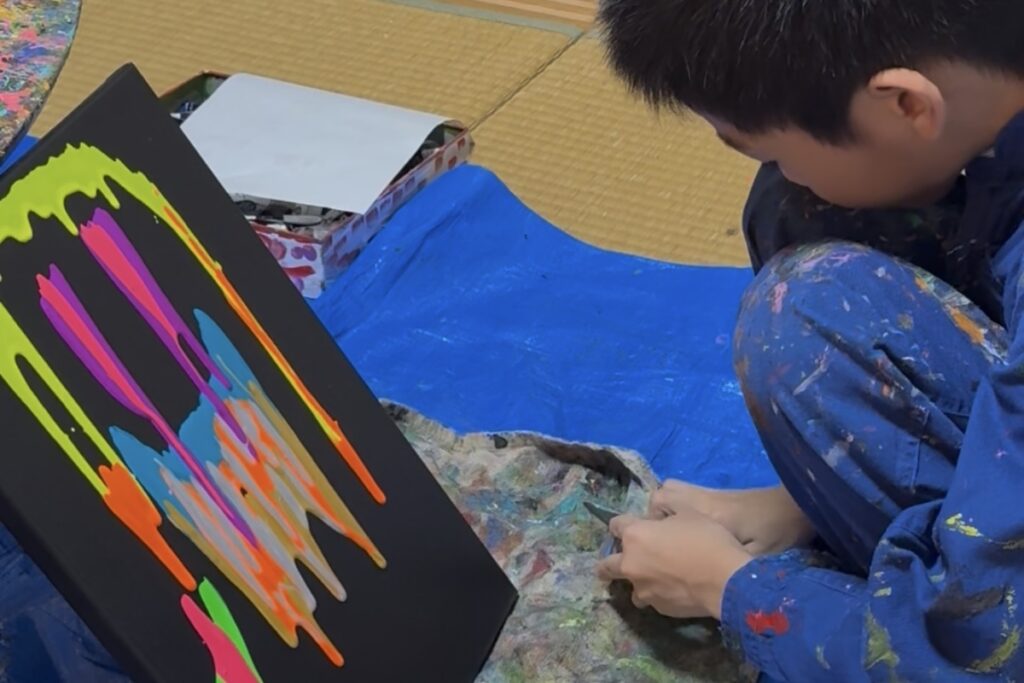 黒いキャンバスに垂れた蛍光色の絵の具を見つめるAKASHI(9歳)の横顔。静かで穏やかな制作後のひととき。