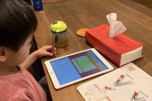 タブレットで英語の勉強をする3歳のAKASHI。机の上にはワークブックとティッシュケースがある。