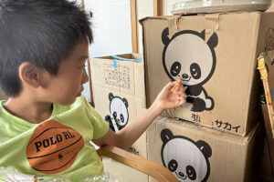 引っ越しの段ボールに描かれたパンダに、芋けんぴを差し出すAKASHI。