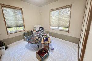 白いシートを敷いた明るい部屋に、絵の具や筆が並ぶアトリエの様子。