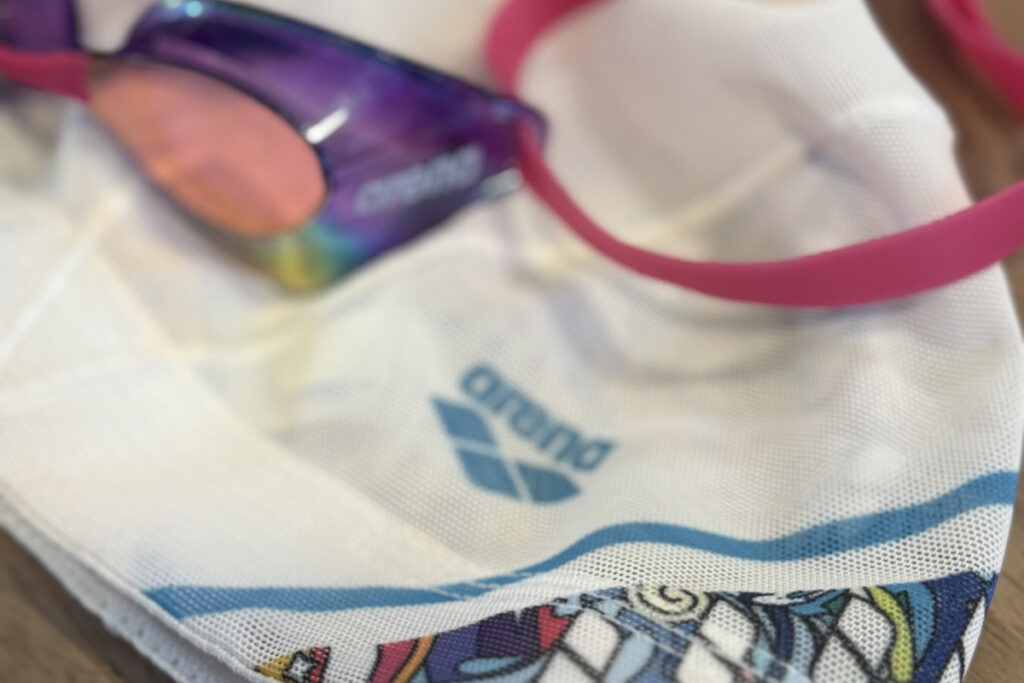 ピンクのゴーグルとarenaのスイムキャップが並ぶ様子。光がやさしく反射して、これからの新しい挑戦を感じさせる。