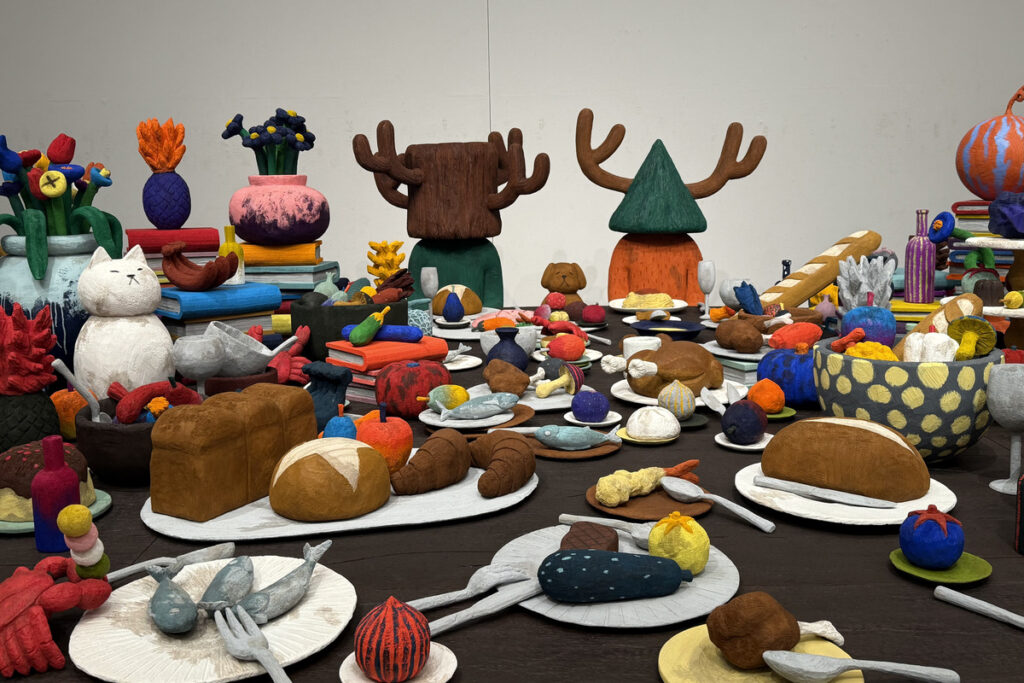 平子雄一展のカラフルな立体作品。パンや魚、果物などの食べ物が並ぶテーブルの作品。