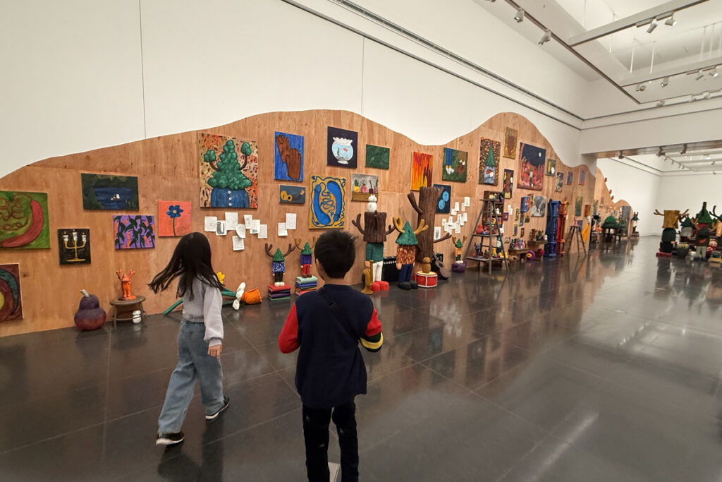 平子雄一展の展示室で、壁一面の作品を眺めながら歩くAKASHIとRIRI。