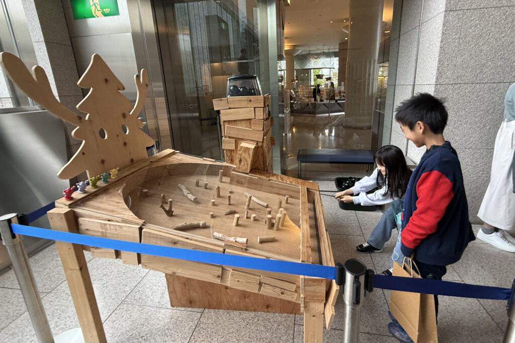 岡山県立美術館の平子雄一展で、木製のガチャガチャ型作品を楽しむAKASHIとRIRI。