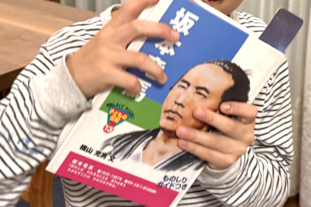 学校の図書館で借りた坂本龍馬の本を手にするAKASHI。興味津々にページを開いている様子。